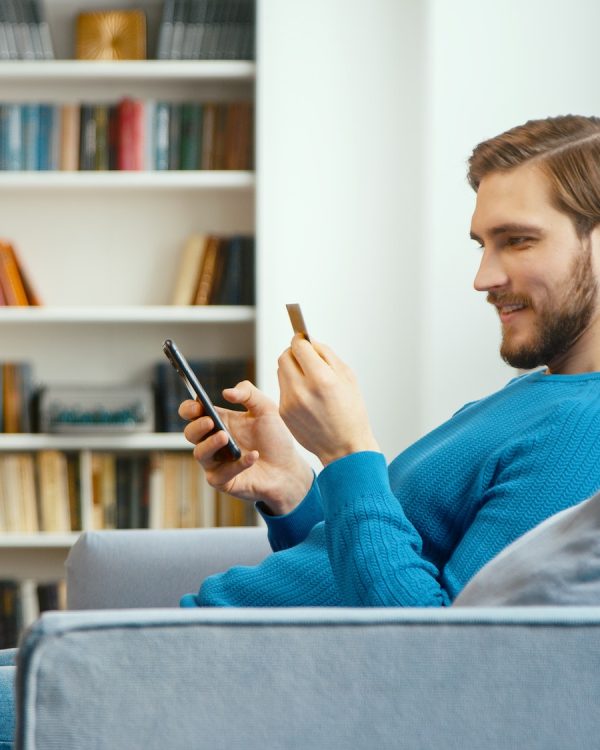 young-man-looks-at-bank-card-in-hand-and-enters-digits-to-smartphone.jpg